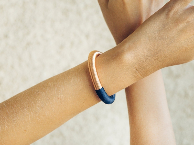 Pu&ograve; includere: Un braccialetto rigido in rame e blu scuro. Il braccialetto &egrave; realizzato con un sottile filo di rame avvolto attorno a una fascia blu scuro.