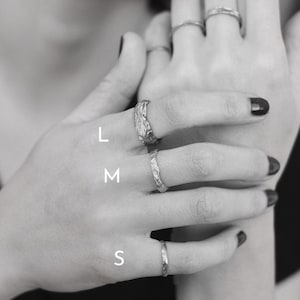 May include: A set of three silver rings, labeled L, M, and S, on a hand. The rings are textured and have a hammered finish.