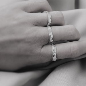 May include: Three silver rings with a textured, wavy design. The rings are stacked on a finger.