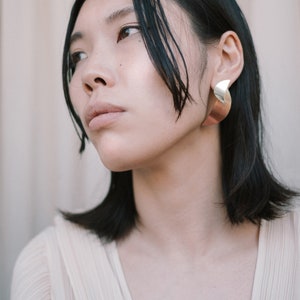 May include: A woman with short black hair wearing a white v-neck top and gold hoop earrings.