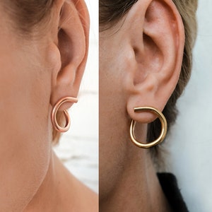 May include: A split image shows two earrings. On the left, a rose gold earring is looped. On the right, a gold hoop earring is worn. The text "two ways to wear" is at the bottom.