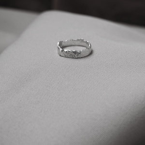 May include: A silver ring with a textured, irregular, mountain-like design.