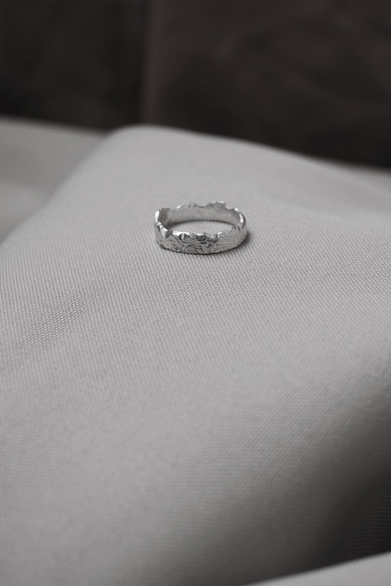 May include: A silver ring with a textured, irregular, mountain-like design.