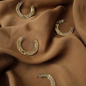 May include: Four gold hoop earrings with a textured hammered finish. The earrings are displayed on a brown fabric background.