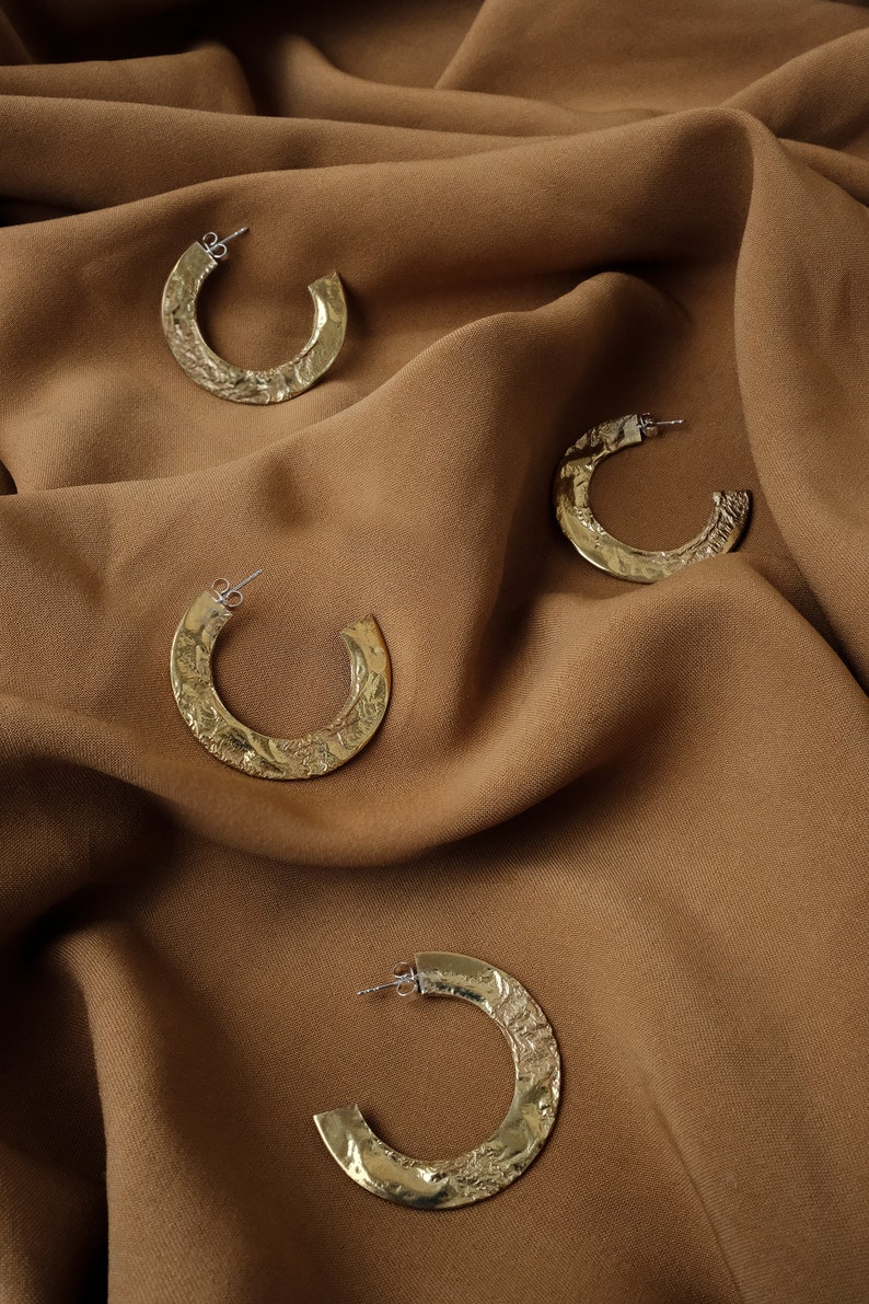 May include: Four gold hoop earrings with a textured hammered finish. The earrings are displayed on a brown fabric background.