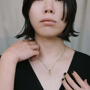 Peut inclure: Une femme aux cheveux noirs courts portant un haut noir &agrave; col en V et un collier en cha&icirc;ne dor&eacute;e avec un petit pendentif.