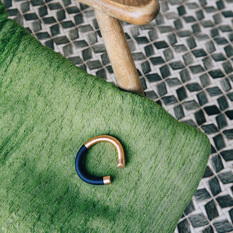 Pu&ograve; includere: Un braccialetto dorato e blu navy su una superficie di tessuto verde.