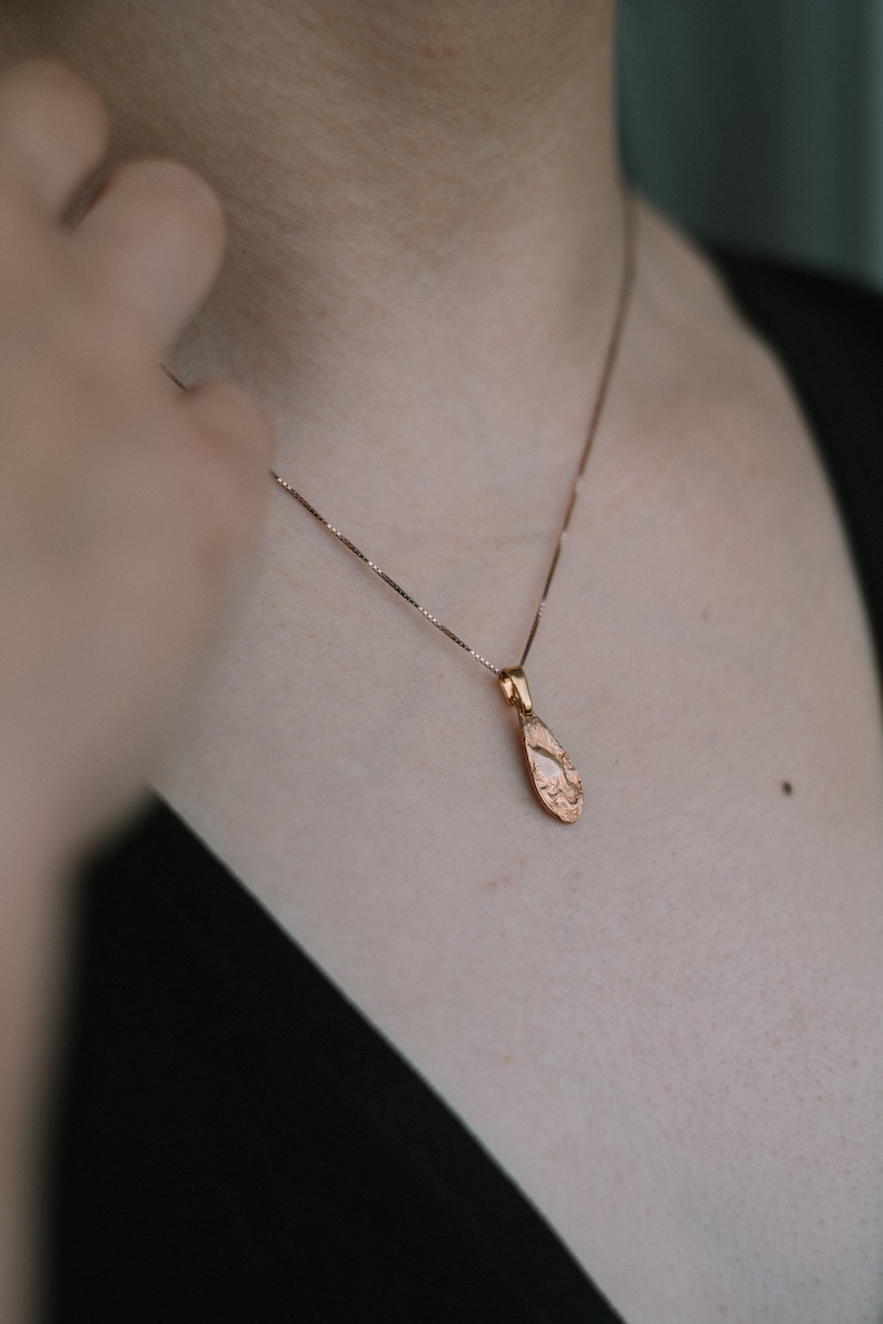Peut inclure: Un collier d&eacute;licat en cha&icirc;ne dor&eacute;e avec un pendentif en forme de larme textur&eacute;.