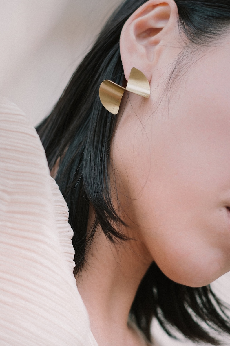 May include: A pair of gold-toned earrings with a twisted, abstract design. The earrings are made of metal and have a polished finish.