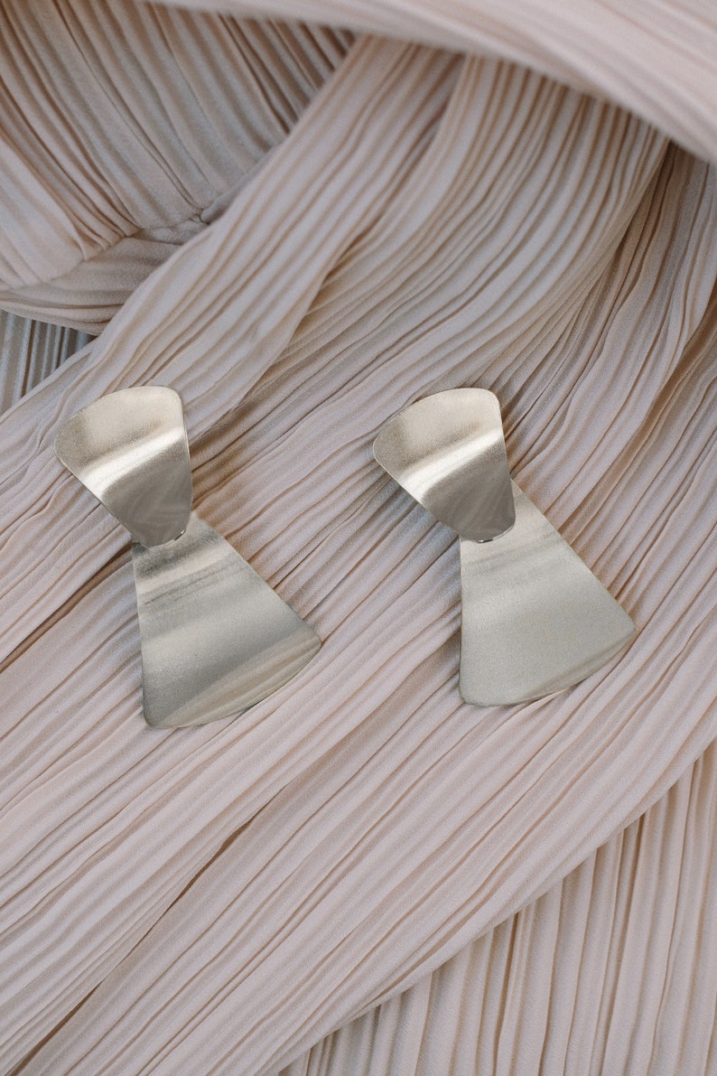 Puede incluir: Un par de pendientes geom&eacute;tricos plateados con un dise&ntilde;o asim&eacute;trico &uacute;nico. Los pendientes est&aacute;n hechos de un metal liso y brillante y tienen una est&eacute;tica moderna y minimalista.