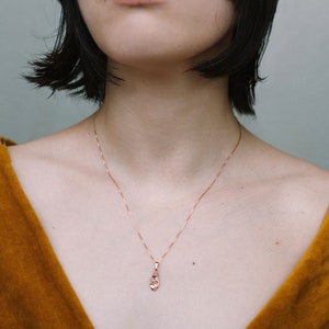 Peut inclure: Une femme portant un haut jaune moutarde avec un collier d&eacute;licat en cha&icirc;ne dor&eacute;e orn&eacute; d'un petit pendentif textur&eacute;.