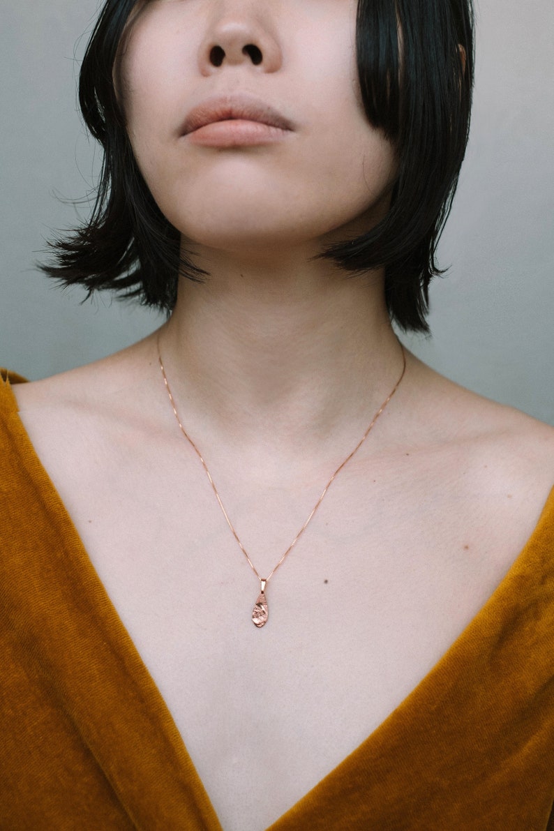 Peut inclure: Une femme portant un haut jaune moutarde avec un collier d&eacute;licat en cha&icirc;ne dor&eacute;e orn&eacute; d'un petit pendentif textur&eacute;.