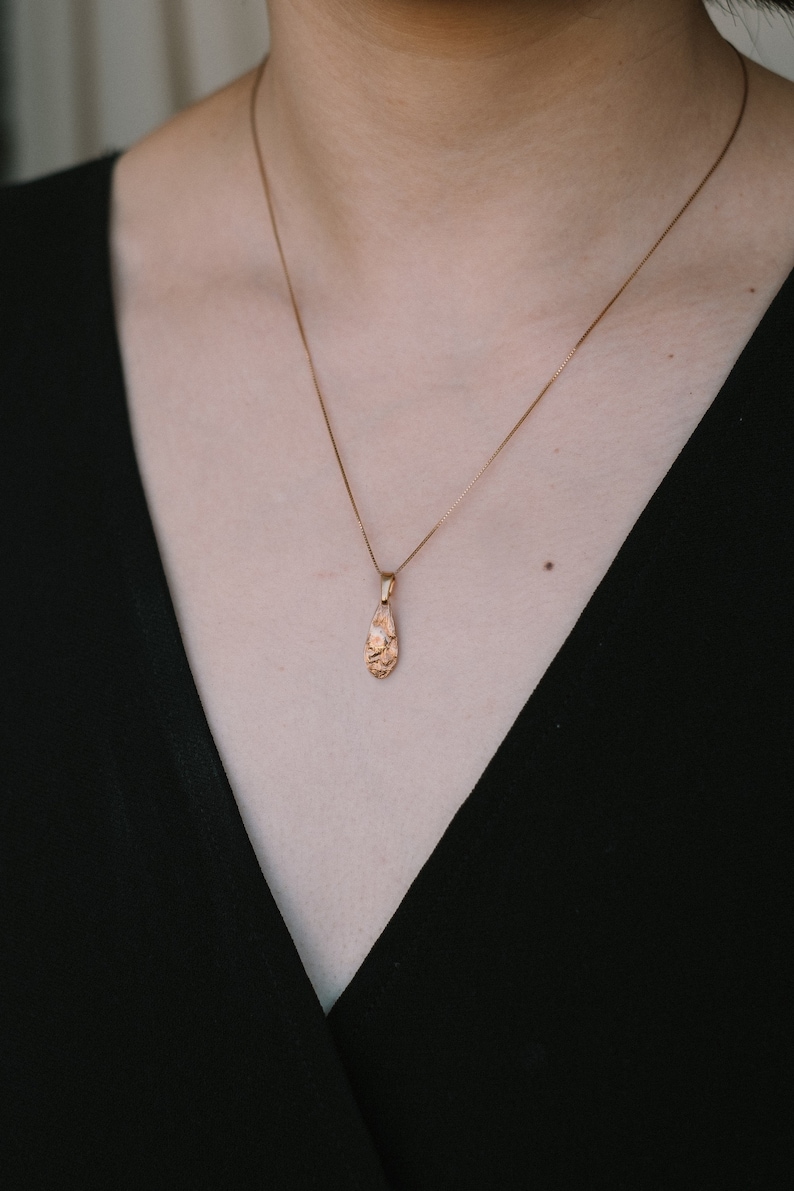 Peut inclure: Un collier en cha&icirc;ne dor&eacute;e avec un pendentif en forme de larme textur&eacute;.