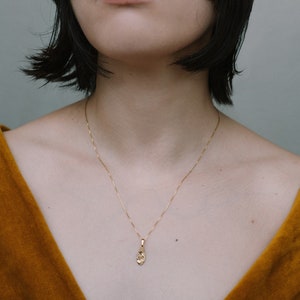 Peut inclure: Une femme portant un haut en velours jaune moutarde avec un collier en cha&icirc;ne dor&eacute;e et un petit pendentif en or.