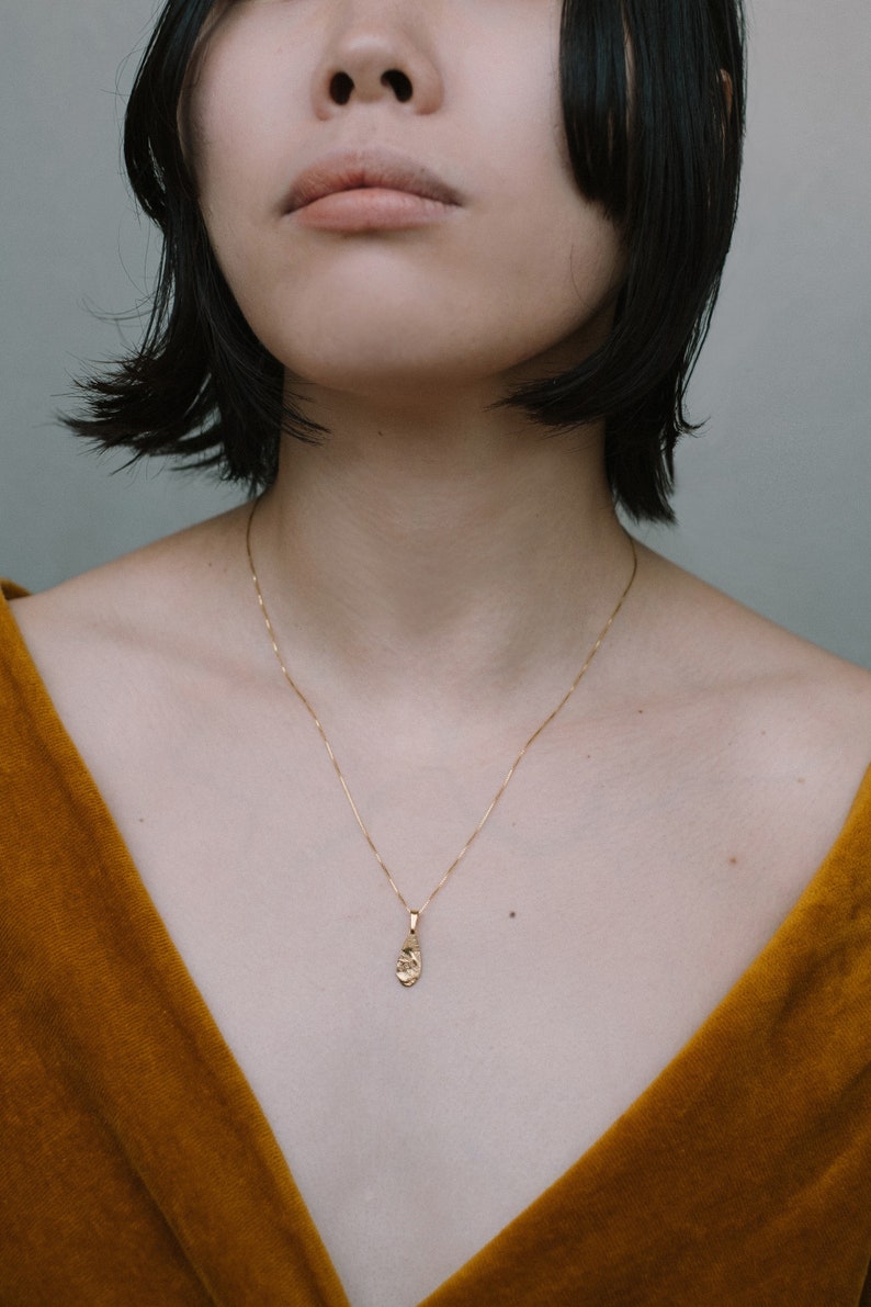 Peut inclure: Une femme portant un haut en velours jaune moutarde avec un collier en cha&icirc;ne dor&eacute;e et un petit pendentif en or.