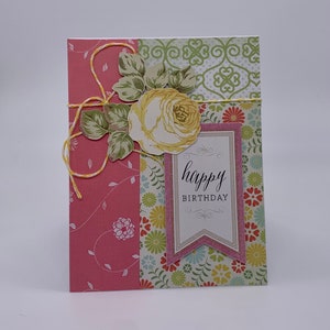 May include: A pink and green patterned card with a yellow rose and leaves. The card has a pink banner with the text "happy birthday" in black script.