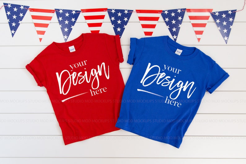 May include: Two blank t-shirts, one red and one blue, laid out on a white wood background. The shirts have the text "Your Design Here" written on them in white. A red, white, and blue bunting hangs above the shirts.
