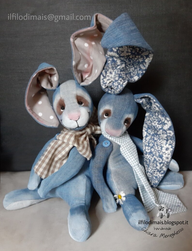 May include: Two denim blue bunny plushies with white polka dot ears and floral patterned ears. One bunny is wearing a brown and white checkered scarf and the other is wearing a white and blue checkered scarf. The bunnies are sitting on a gray surface. The text "ilfilo di mais.blogspot.it" is on the bottom right corner of the image.