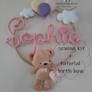 Puede incluir: Letrero de nombre de bebé hecho a mano con el nombre "Sophie" en hilo rosa, un osito de peluche, globos y nubes. El letrero es parte de un kit de costura con un tutorial para un lazo de nacimiento.