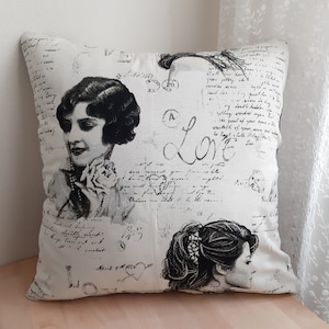 Può includere: Un cuscino bianco con un design vintage in bianco e nero con due volti di donne, la parola "Love" e testo scritto a mano. Il cuscino ha uno sfondo bianco con testo e immagini nere.