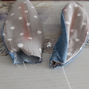 May include: Two gray fabric bunny ears with white polka dots and blue denim trim. The ears are sewn together at the base and have a white thread attached.