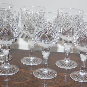May include: A set of six clear glass goblets featuring a diamond-cut pattern on the bowl, a smooth stem, and a circular base with a radial starburst design. Each glass has a rounded rim and a sturdy foot, reflecting light through the faceted glass.