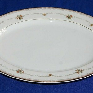May include: An oval serving platter. The white surface is framed by a decorative border with small floral motifs and a gold trim. The platter is designed for serving food and is suitable for special occasions.