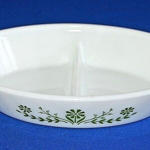 May include: White oval divided baking dish with green floral design. The dish has two sections and is made of white ceramic.