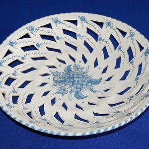 May include: White ceramic basket with a lattice design and blue floral accents. The rim and centre of the basket feature hand-painted blue flowers and vines. The basket is round and has a decorative, openwork design.
