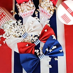 Könnte beinhalten: Eine festliche Anordnung mit roten, weißen und blauen Fliegen und Popcorn. Die Fliegen haben einen gestreiften Akzent. Popcorn quillt aus klassischen Popcornboxen. Der Hintergrund hat rote und weiße Streifen.