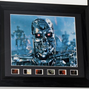 May include: A framed movie poster featuring a close-up of the Terminator, a cyborg with red eyes, in a futuristic setting. The poster includes a row of film cell frames.
