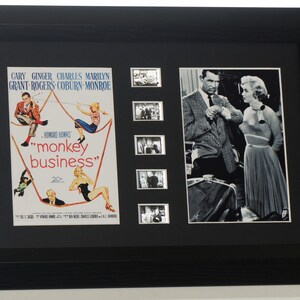 Könnte beinhalten: Gerahmtes Schwarz-Weiß-Filmposter und Filmstills aus dem Film "Monkey Business" mit Cary Grant, Ginger Rogers, Charles Coburn und Marilyn Monroe. Das Poster zeigt farbenfrohe Illustrationen, während die Stills in Schwarzweiß gehalten sind.