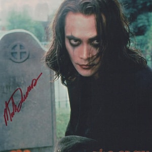 May include: A promotional image for "The Crow: Stairway to Heaven" featuring a person with dark makeup and long, dark hair. The person is in front of a tombstone. The film's title is at the bottom, and a signature is visible.