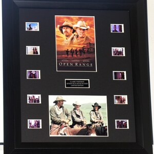 May include: Framed "Open Range" movie poster with film stills. The poster features actors in cowboy hats, with the title in white letters. The frame is black, and the artwork is mounted on a black background.