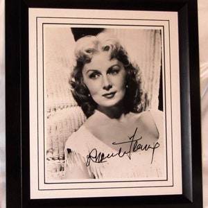 Może przedstawiać: Czarno-białe zdjęcie kobiety o kręconych włosach, w białej sukience. Zdjęcie jest podpisane "Ann Blyth".