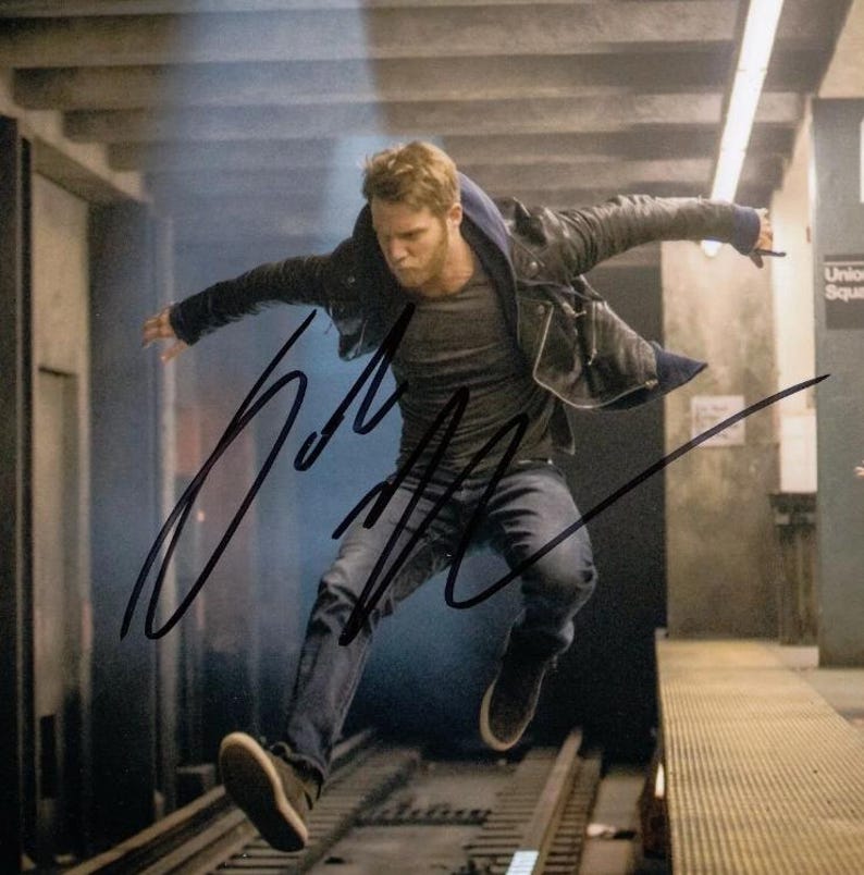 May include: A man wearing a black leather jacket and jeans jumps in mid-air with his arms outstretched. The image is signed with the name "John" in black ink.