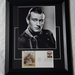 Peut inclure: Portrait encadré en noir et blanc de John Wayne, avec un timbre et une enveloppe sur le thème des cow-boys. Le cadre est noir, et le portrait est centré avec un passe-partout blanc.