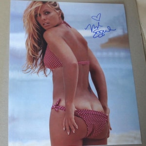 May include: A photograph of a person wearing a red polka dot bikini. The bikini top has halter straps, and the bottoms have a bow on the side. The person is fair-skinned with long blonde hair. A signature is visible in the upper right corner.