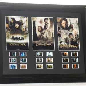 May include: A black framed artwork displaying three film posters from "The Lord of the Rings" trilogy. Below each poster are several film stills. The posters and stills are in colour.