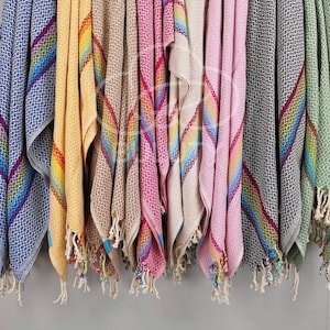 May include: A collection of colorful striped towels with fringe edges. The towels are hanging on a wall and are made of a soft, absorbent material.
