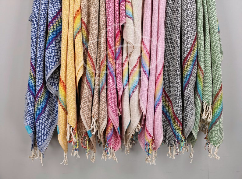 May include: A collection of colorful striped towels with fringe edges. The towels are hanging on a wall and are made of a soft, absorbent material.