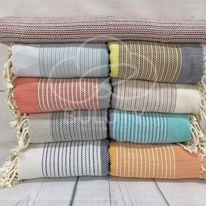May include: A stack of eight striped towels with fringed edges in various colors, including red, blue, yellow, orange, and white.