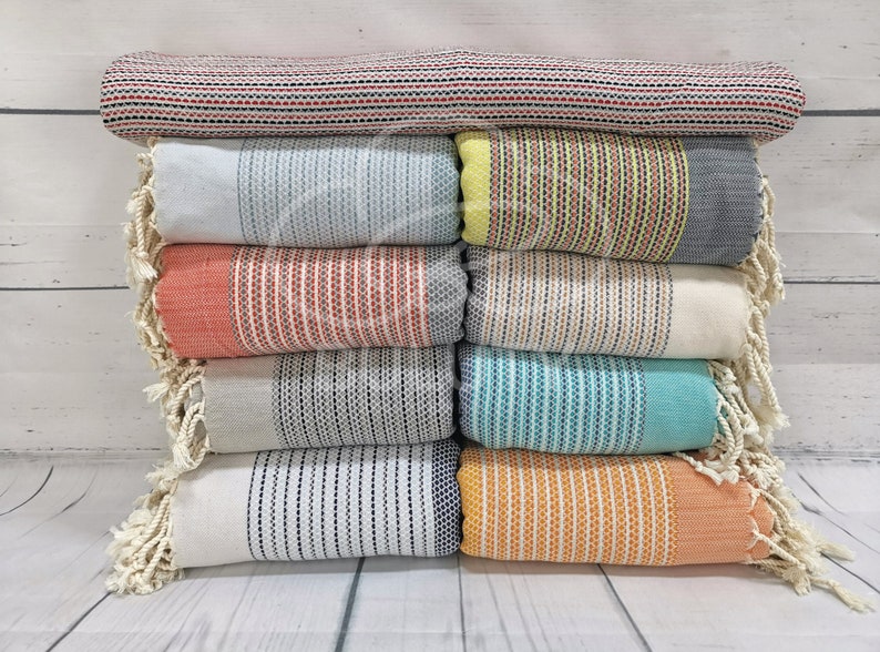 May include: A stack of eight striped towels with fringed edges in various colors, including red, blue, yellow, orange, and white.