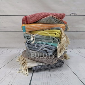 May include: A stack of colorful Turkish towels with fringe, folded and arranged in a pyramid shape. The towels are in shades of red, yellow, green, blue, and gray.