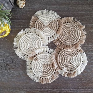 Puede incluir: Conjunto de cinco posavasos redondos de ganchillo con flecos. Los posavasos están hechos en un esquema de color beige y blanco.