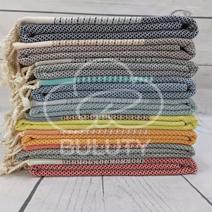 May include: A stack of 12 colorful Turkish towels with fringe. The towels are folded and stacked in a variety of colors, including blue, gray, green, yellow, orange, and red.