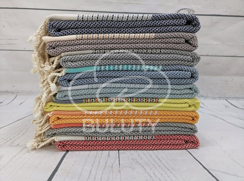 May include: A stack of 12 colorful Turkish towels with fringe. The towels are folded and stacked in a variety of colors, including blue, gray, green, yellow, orange, and red.
