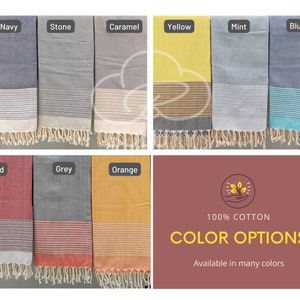 May include: A collection of 100% cotton Turkish towels in various colors, including navy, stone, caramel, yellow, mint, blue, red, grey, and orange. The towels have a woven pattern and fringe edges. 100% COTTON COLOR OPTIONS Available in many colors