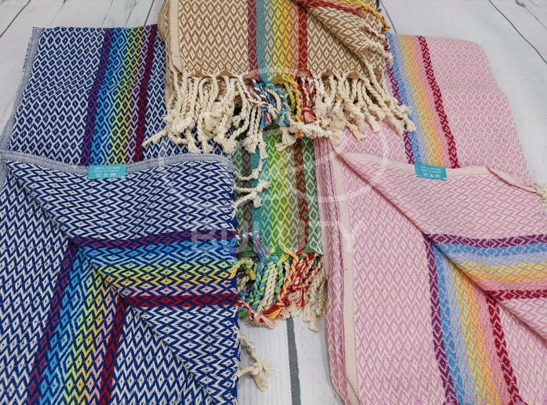 May include: Four colorful striped towels with diamond patterns and fringe. The towels are in shades of blue, pink, brown, and green.