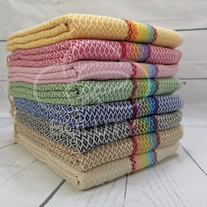 May include: A stack of eight colorful patterned towels with fringed edges. The towels are folded and stacked in a pyramid shape. The towels are made of a soft, absorbent material and are perfect for drying off after a shower or bath.